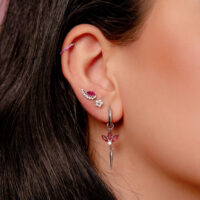 Hopeinen korvakoru korvassa punaisilla kristalleilla ja useilla lävistyksillä yhdessä korvassa