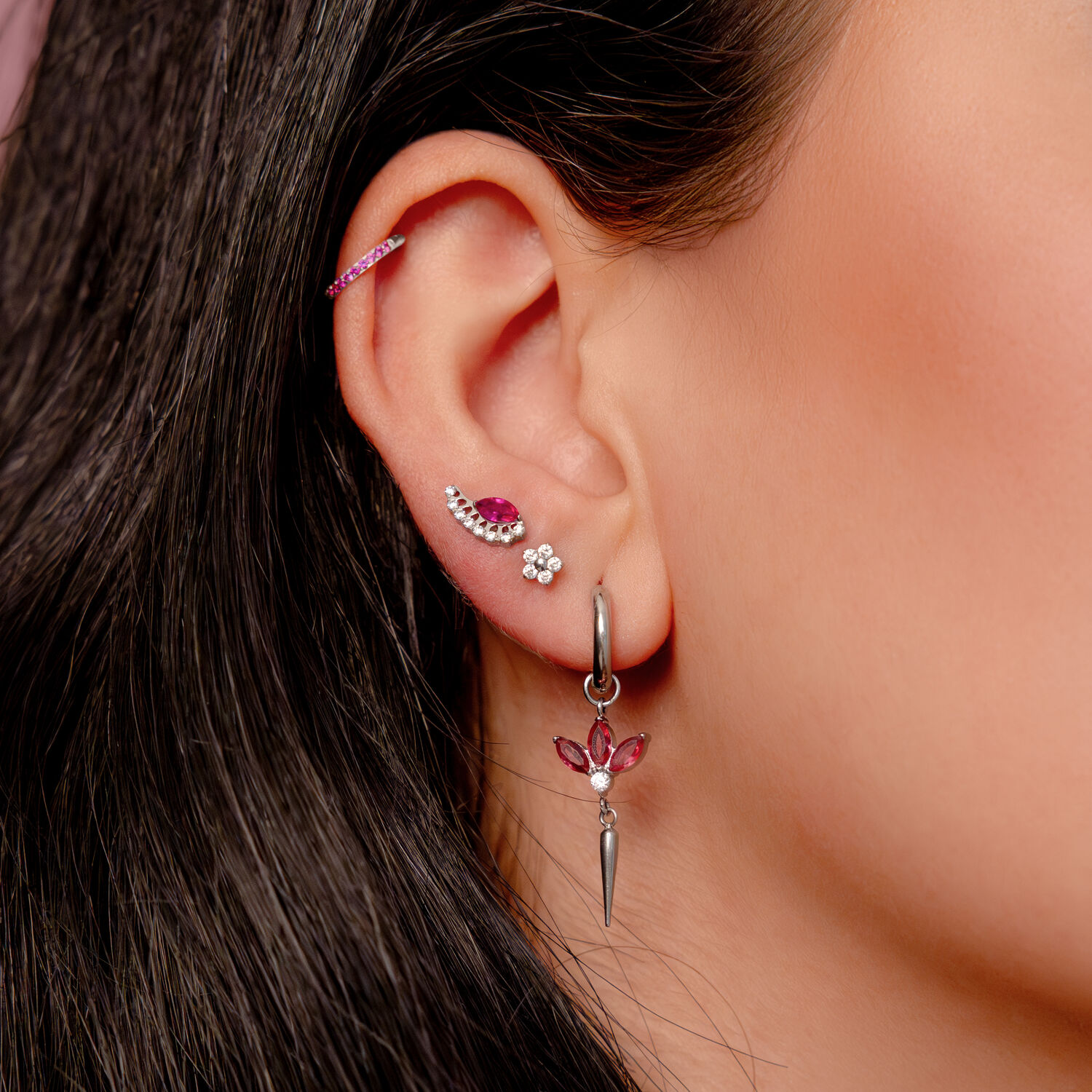 Hopeinen korvakoru korvassa punaisilla kristalleilla ja useilla lävistyksillä yhdessä korvassa