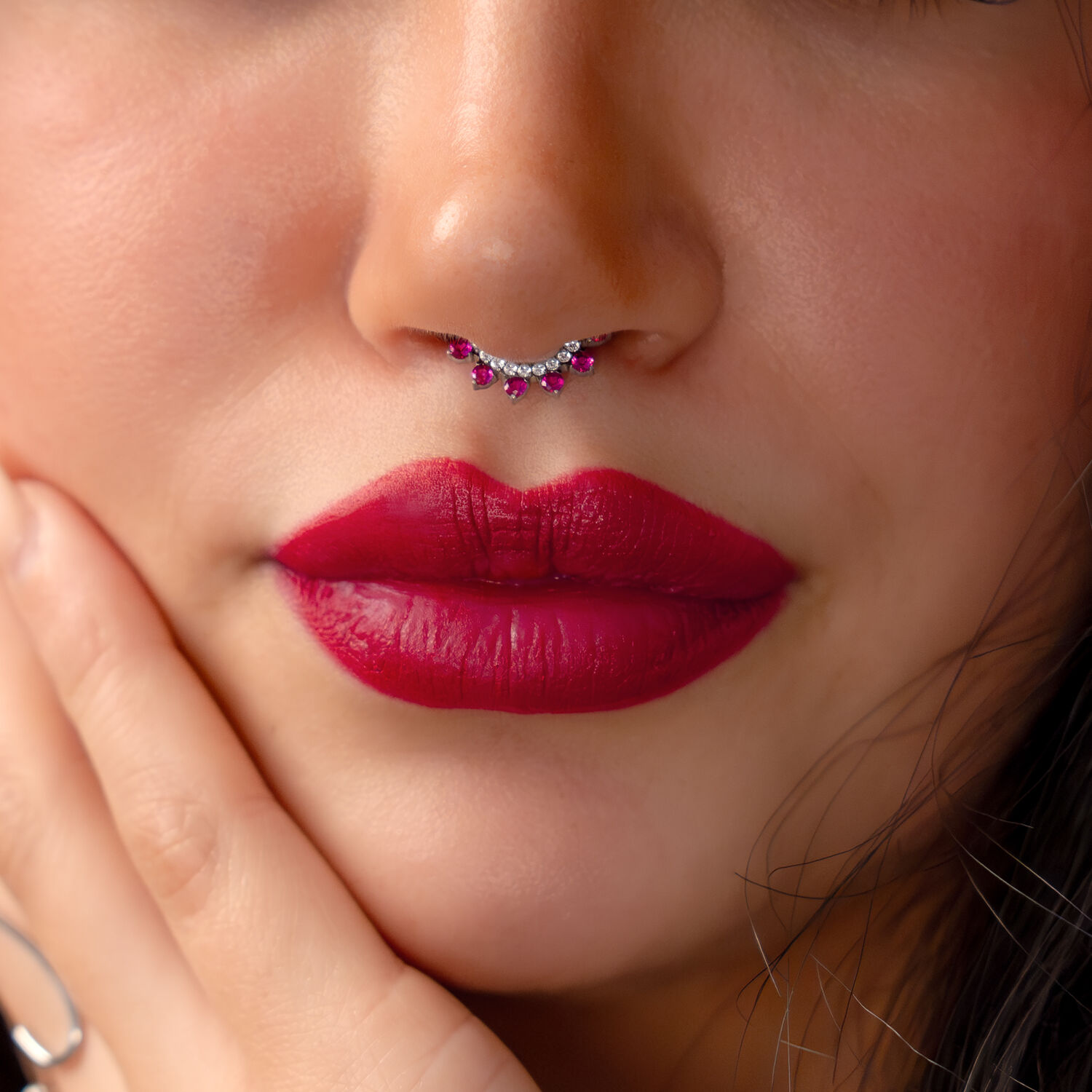 Lähikuva kasvoista, joissa on hopeinen septum-lävistys ja punaisia kristalleja