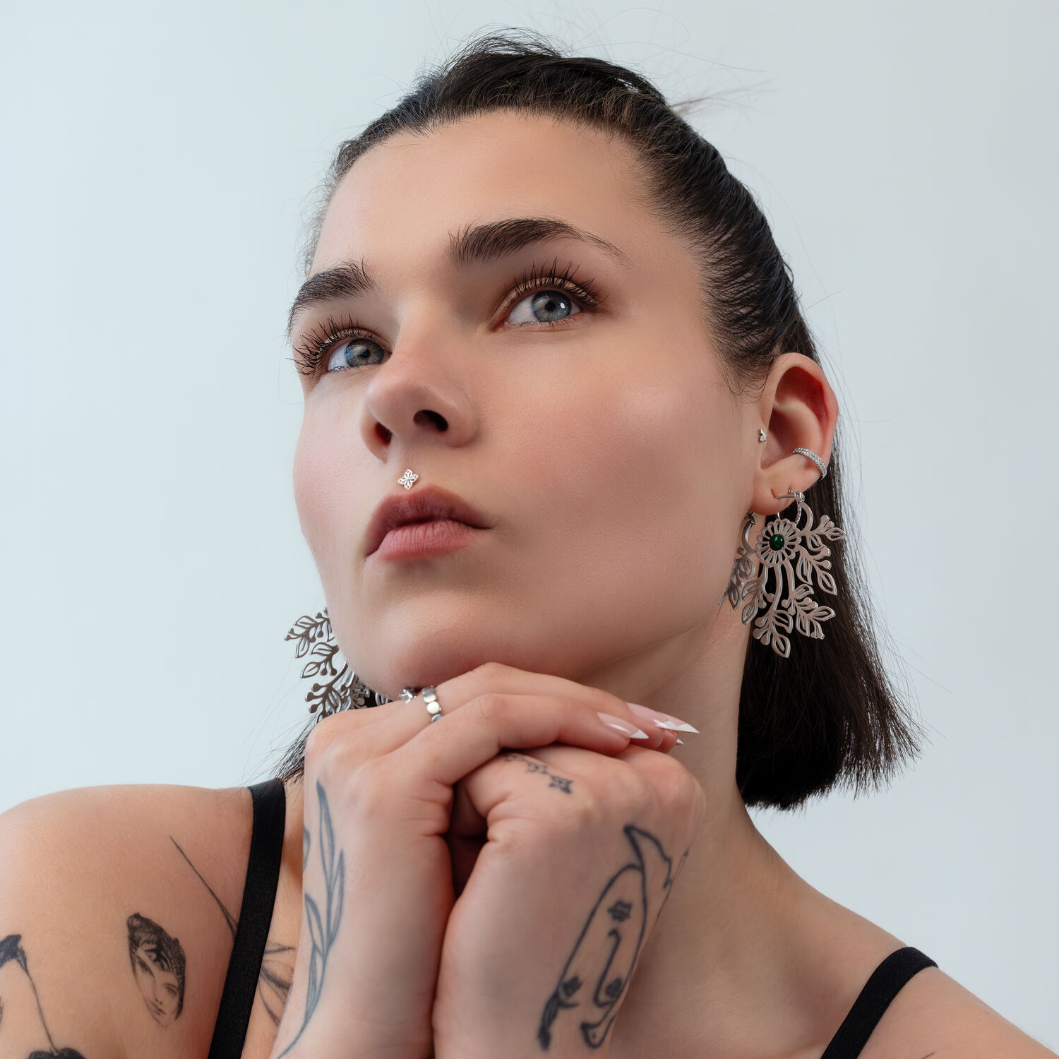 Elegantit kirurginteräksiset korvakorut Nainen lyhyillä hiuksilla käyttää suuria, hienostuneita korvakoruja hopeanvärisestä metallista vaalealla taustalla